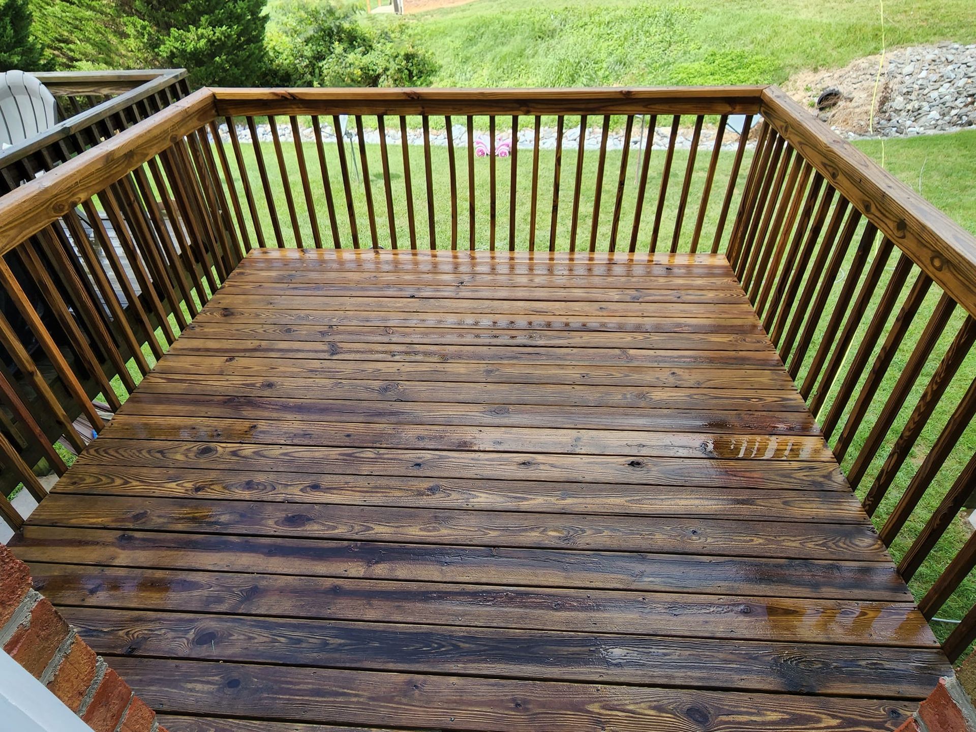 Wooden deck with brown railings and wet, weathered floorboards, outdoors.