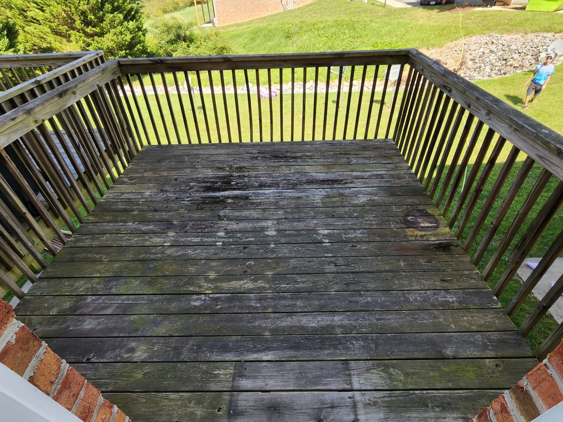 A weathered wooden deck with railing and a grassy background.