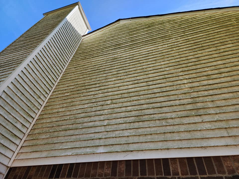 Light green siding with brick foundation and chimney against a blue sky.