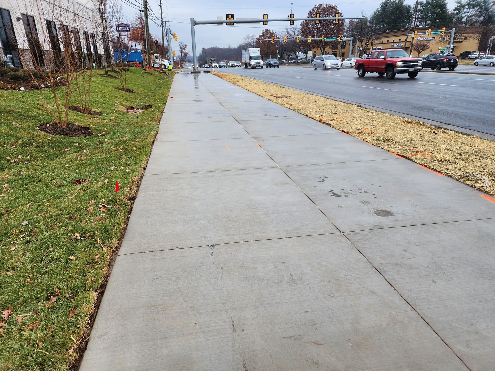 Sidewalk next to road with cars, grass and gravel bed. Overcast day.