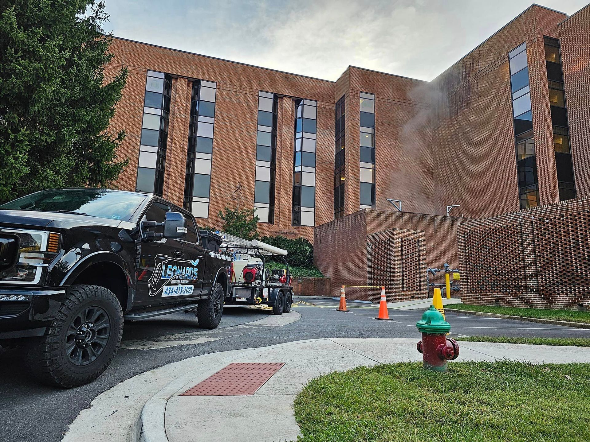 Black truck and sprayer near brick building; fire hydrant in foreground, work zone present.