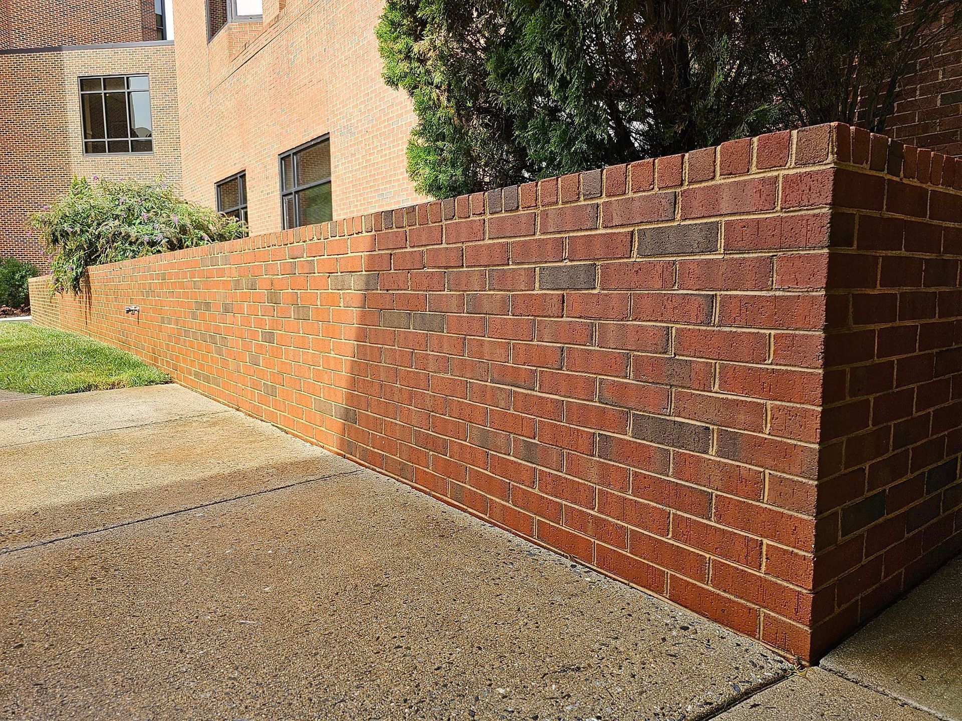 Brick retaining wall slopes down next to a concrete sidewalk, in front of a brick building.