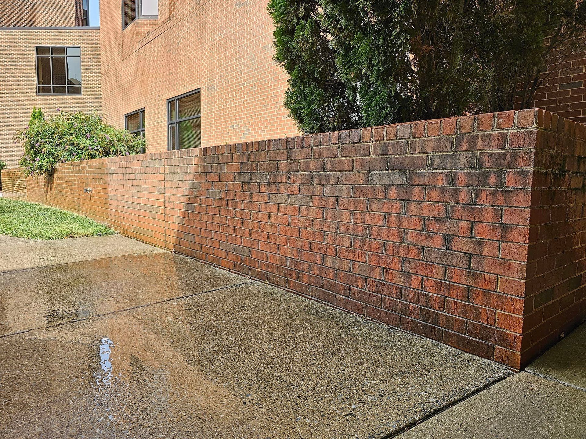 Brick wall with sloping design next to a concrete walkway and building.