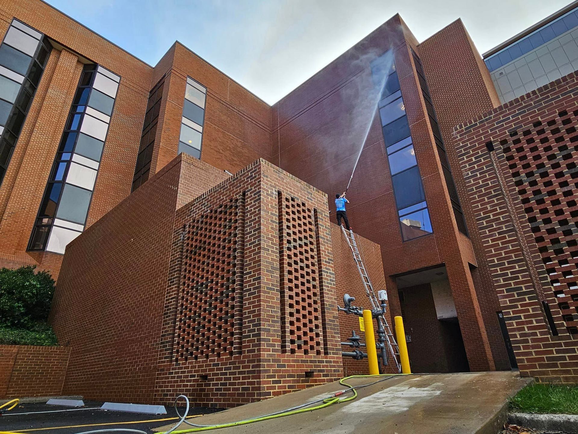 Person on ladder cleaning brick building. Exterior view.