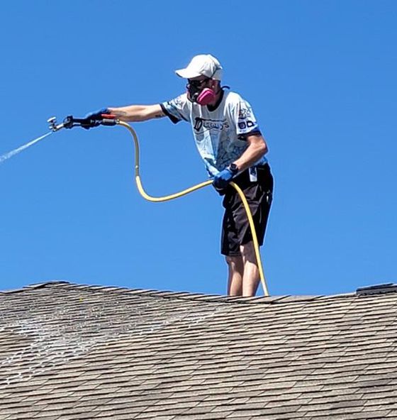 Man on rooftop sprays substance, wearing mask, against blue sky.