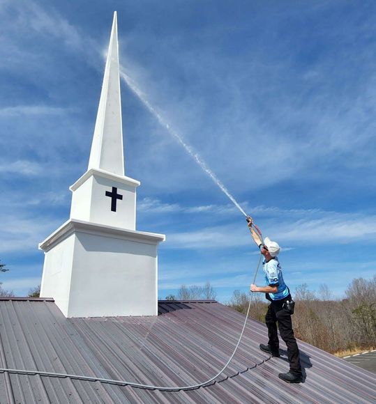 Person on a church roof spraying the steeple with water.