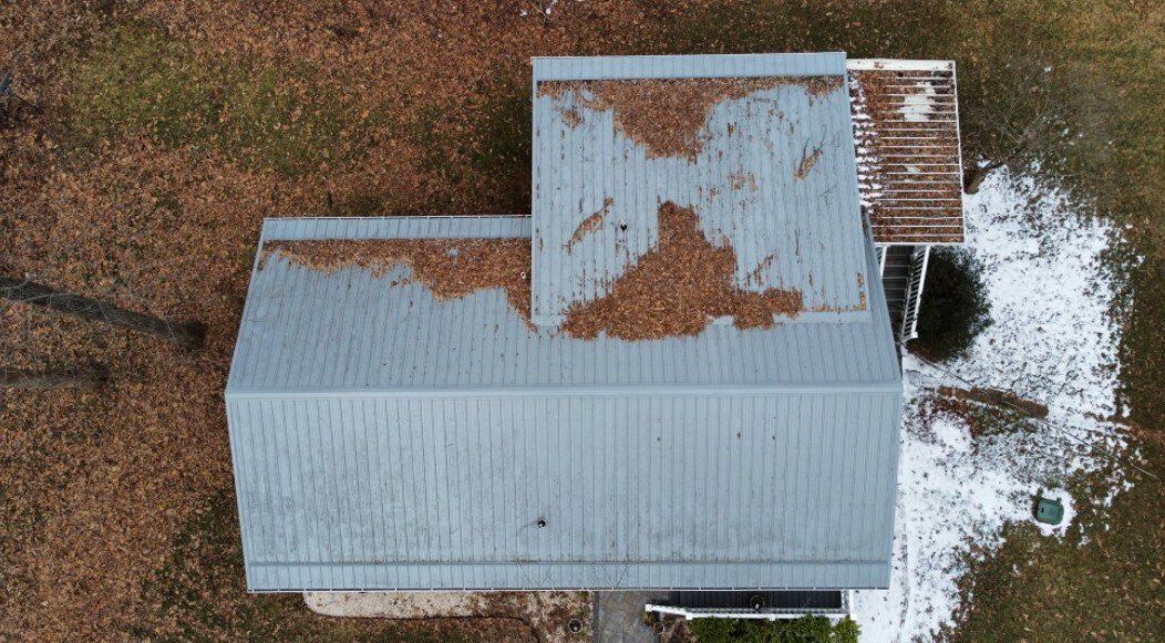 Overhead view of a gray metal-roofed building with brown leaves and patchy snow on the ground.