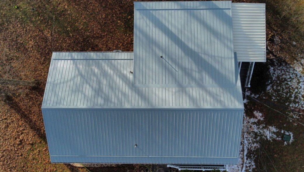 Overhead view of a barn with a metal roof, surrounded by brown leaves and a small patch of snow.
