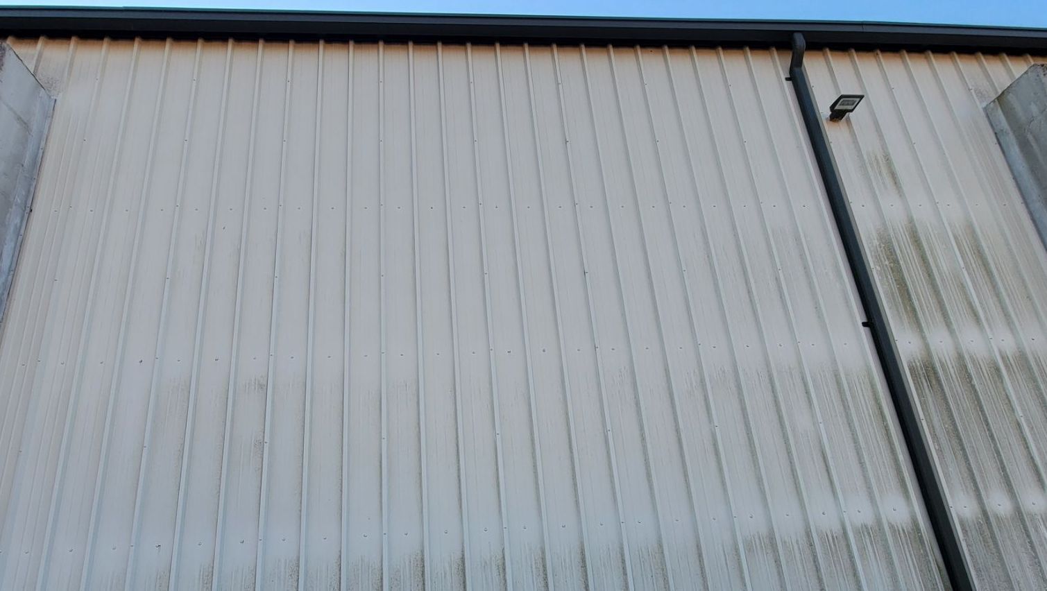 Gray, vertically-paneled building exterior with a black gutter and downspout; some staining.