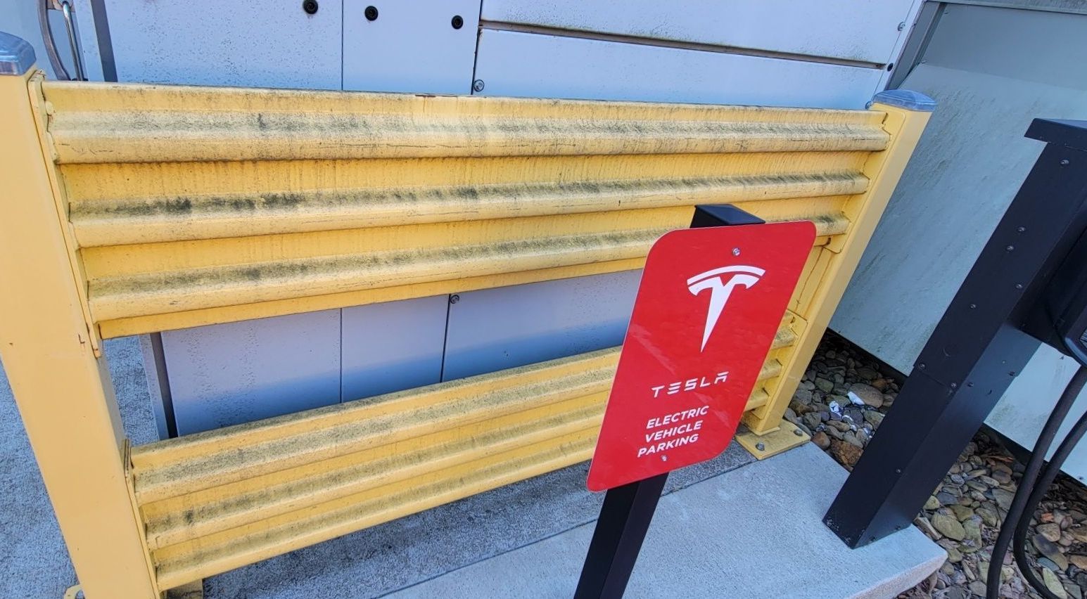 Yellow barrier at a Tesla charging station, red sign with Tesla logo.