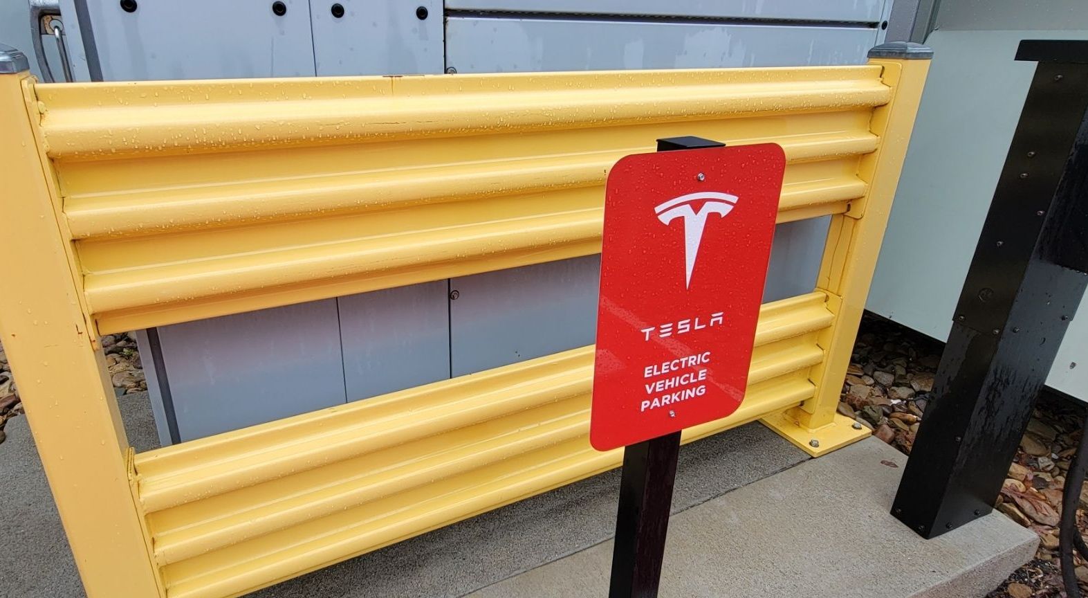 Red Tesla electric vehicle charging station sign in front of a yellow barrier.