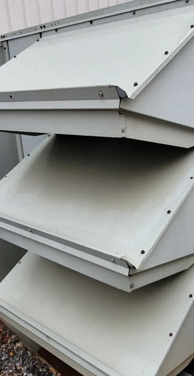 Stack of gray, angled air vents with visible screw heads and a weathered appearance.
