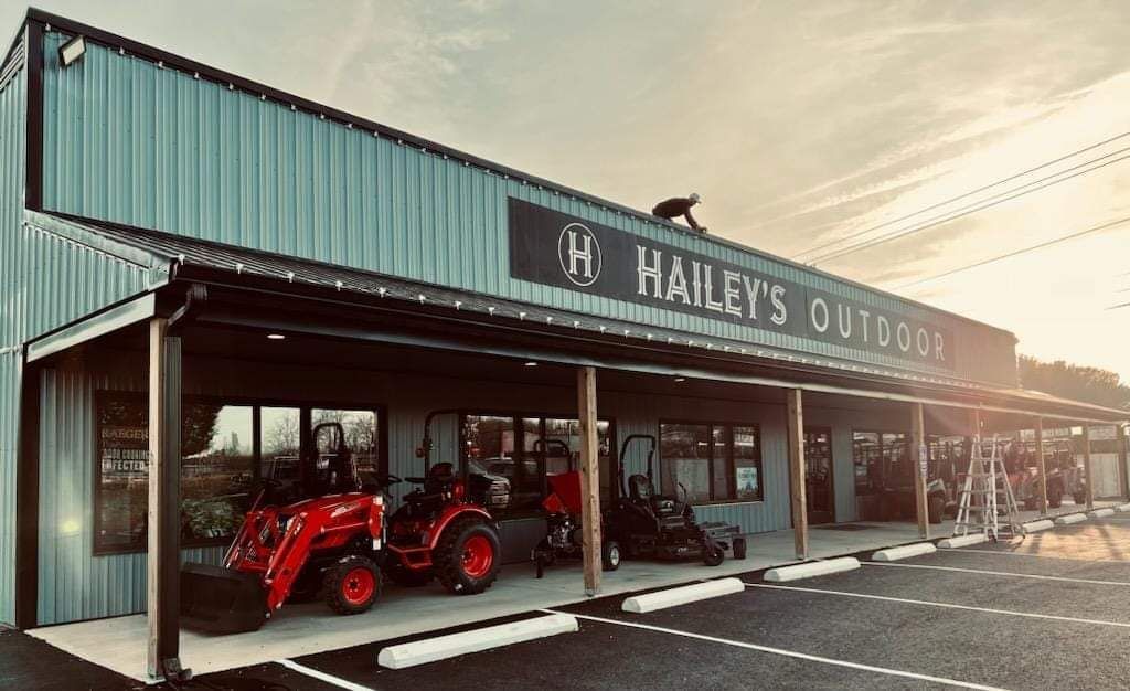Hailey's Outdoors store with tractors and a person on the roof. Blue building with signage.