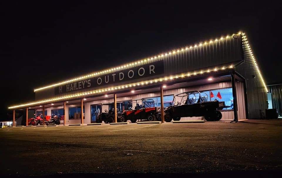 Nighttime view of H Harley's Outdoor store lit up with string lights. Vehicles sit on display in front.