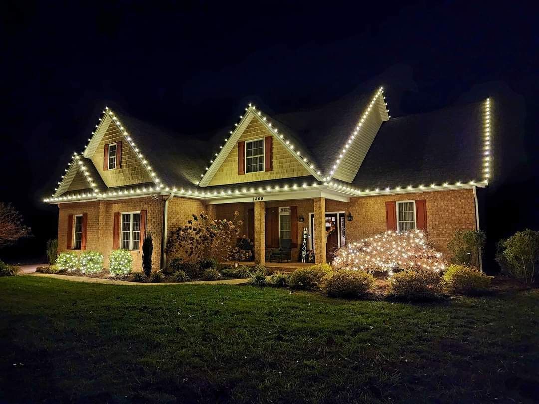 House decorated with white Christmas lights on roof and shrubs.