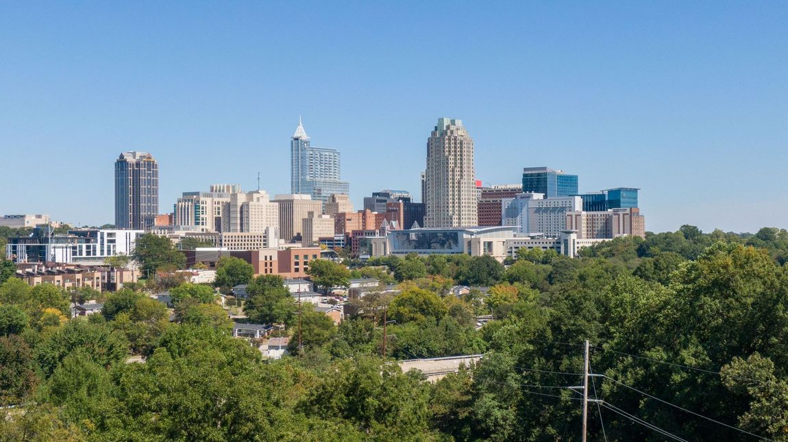 City skyline with tall buildings above dense green trees under a clear blue sky