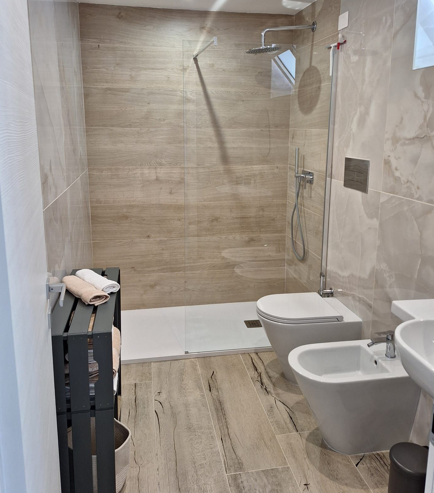 Bagno moderno con due lavandini bianchi, doccia in vetro e pareti rivestite con piastrelle effetto legno.