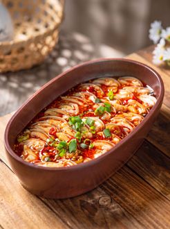 Oval baked dish of sliced potatoes in red sauce, topped with herbs, on a wooden table