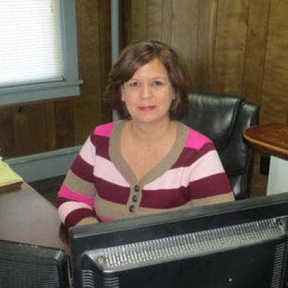 A woman is sitting at a desk in front of a computer monitor.