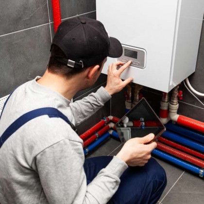 A man is kneeling down in front of a boiler and using a tablet.