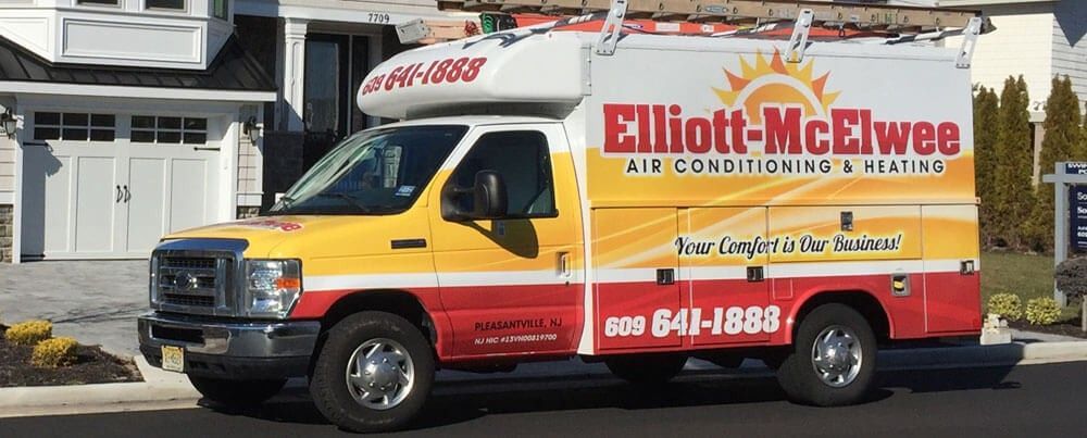 A yellow and red Elliott-Mcelwee van is parked in front of a house.
