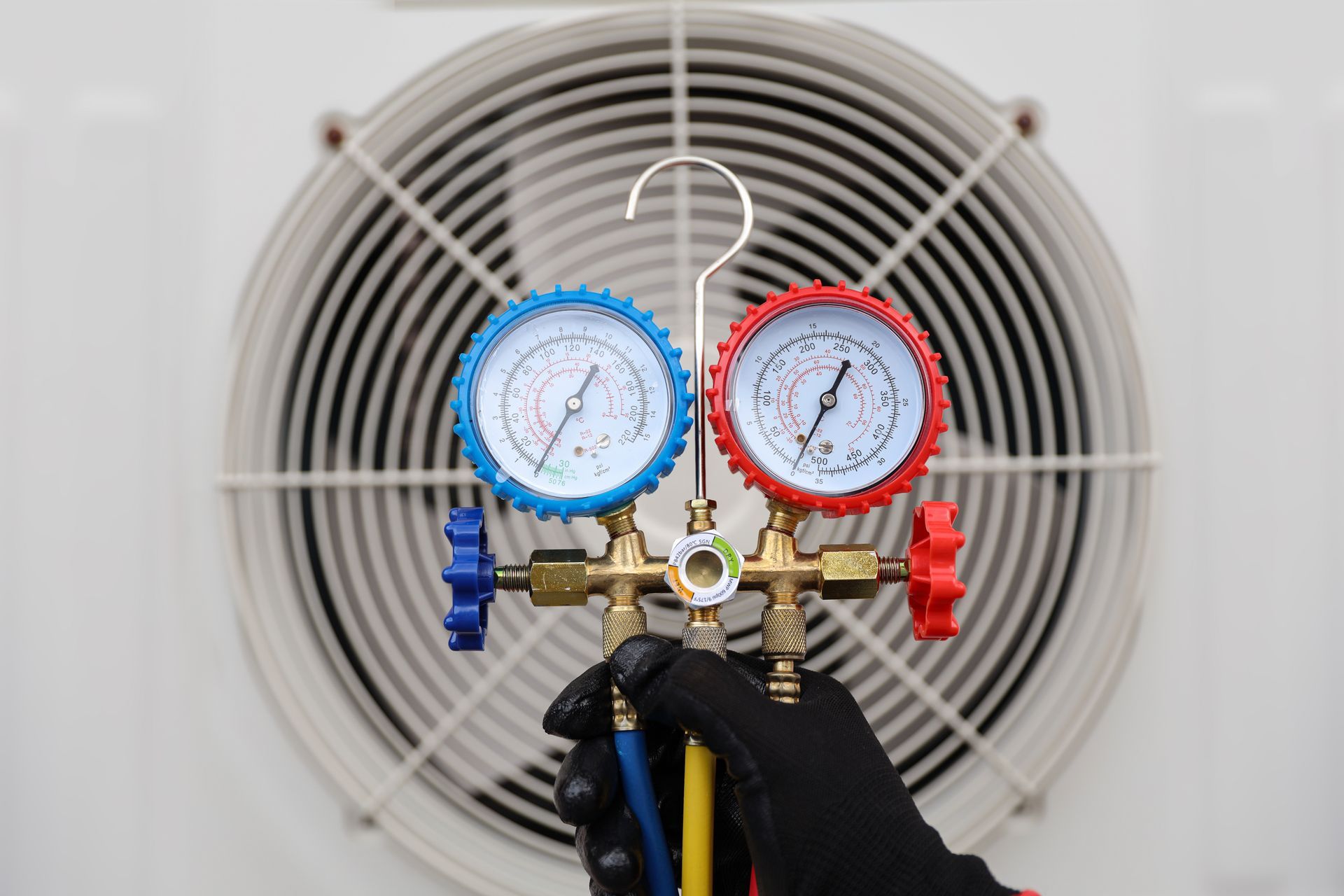 Manifold gauge set connected to an AC unit, with a white fan in the background.