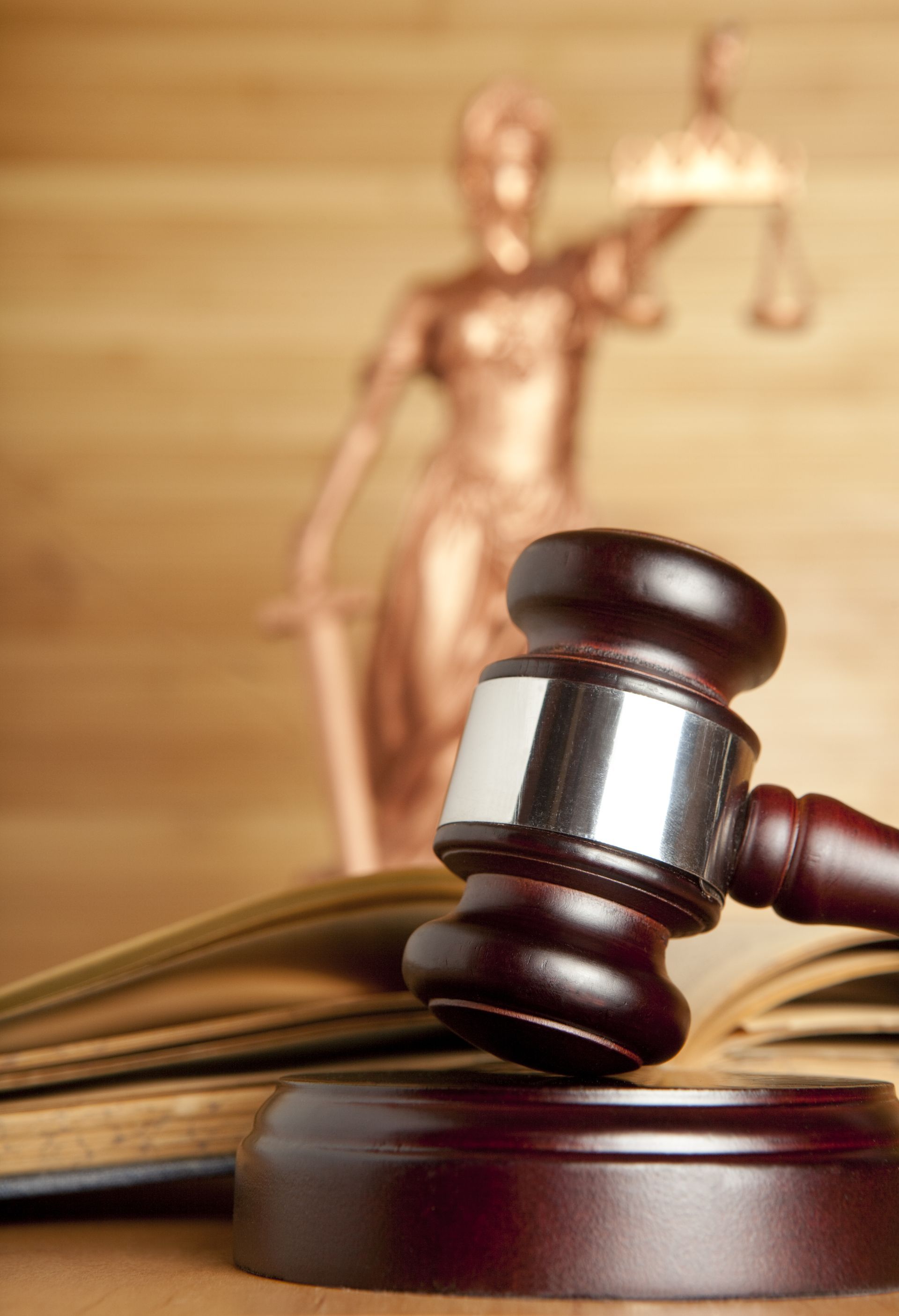 a statue of justice is behind a wooden gavel