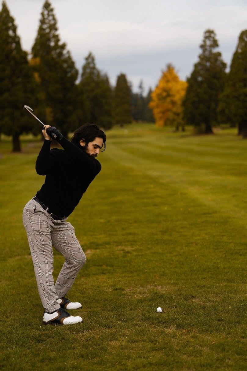 Golfer mid-swing on a green course, with trees and a cloudy sky in the background