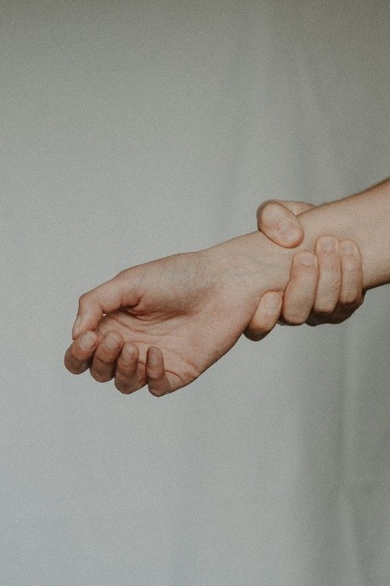A hand gripping another person’s wrist against a plain light background.