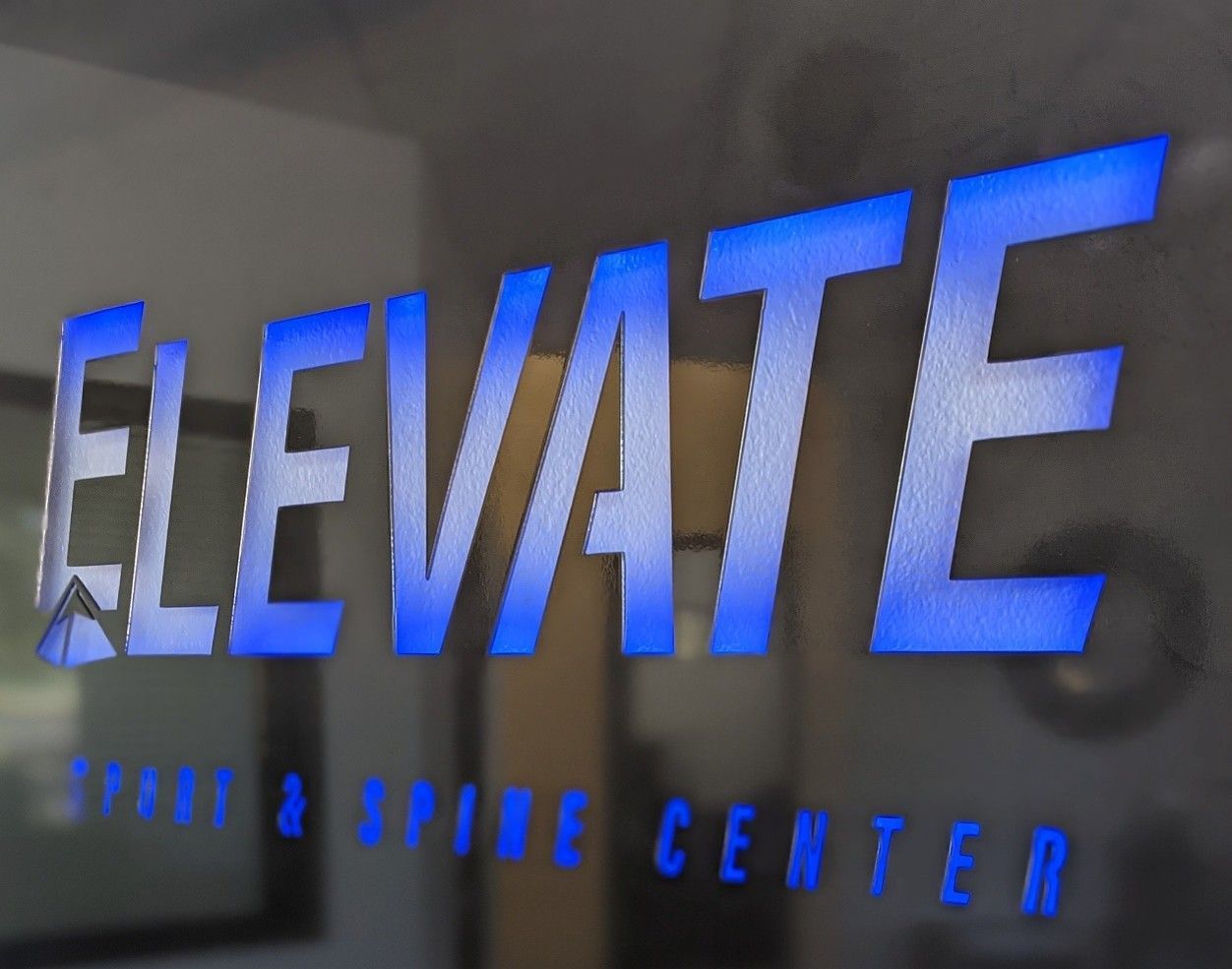 Blue “ELEVATE” sign with smaller “spine & spine center” text on a wall.