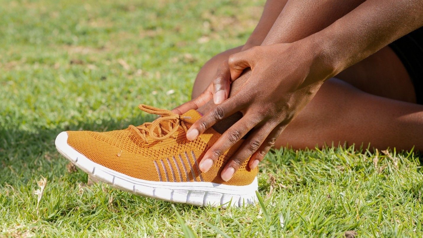 Hands tying an orange knit sneaker on grass outdoors