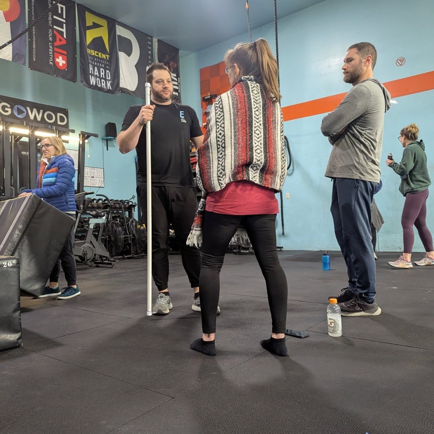 People practicing with staffs in a gym, with mirrors and banners on the wall.