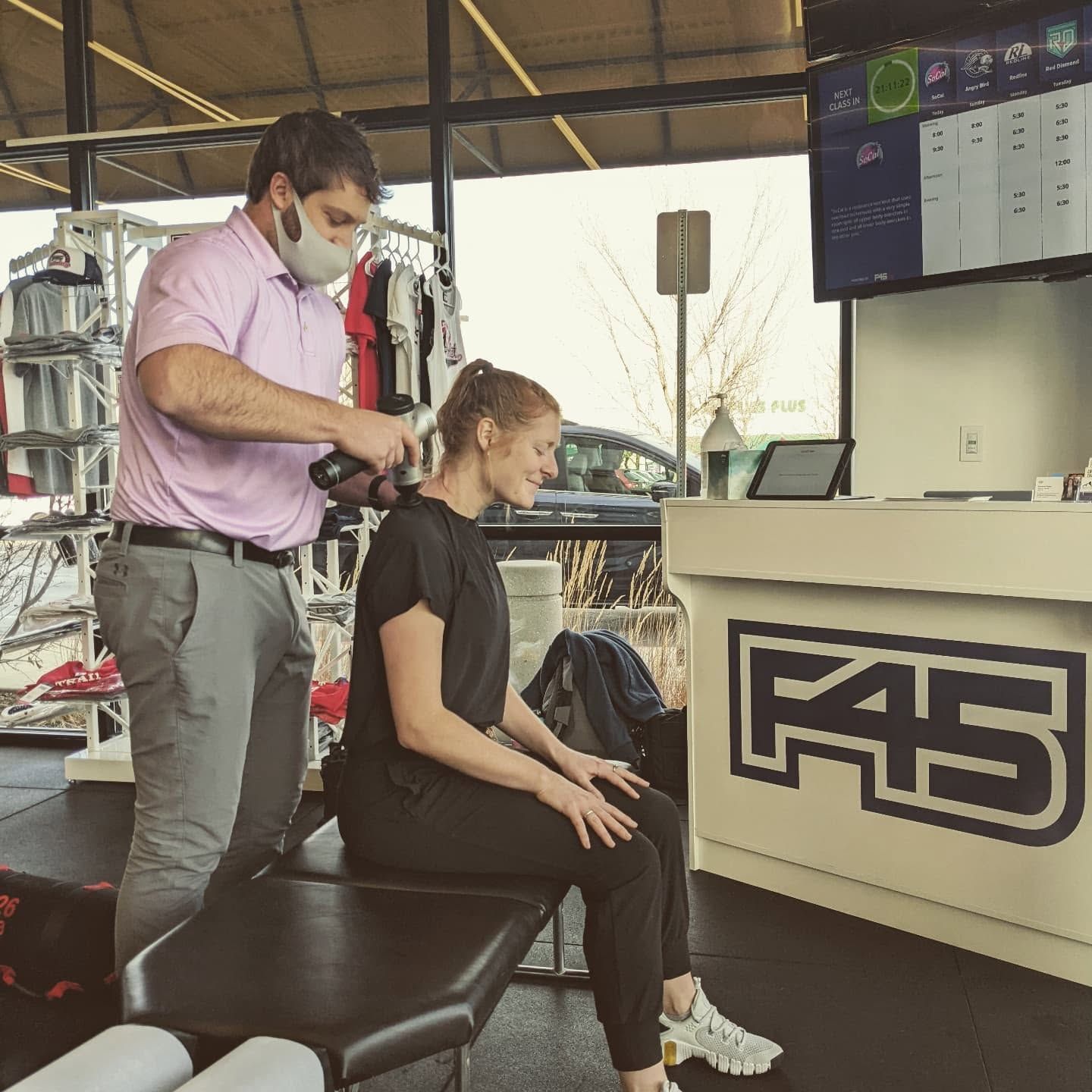 Masked therapist adjusting a seated client’s hair in a modern salon or clinic lounge.