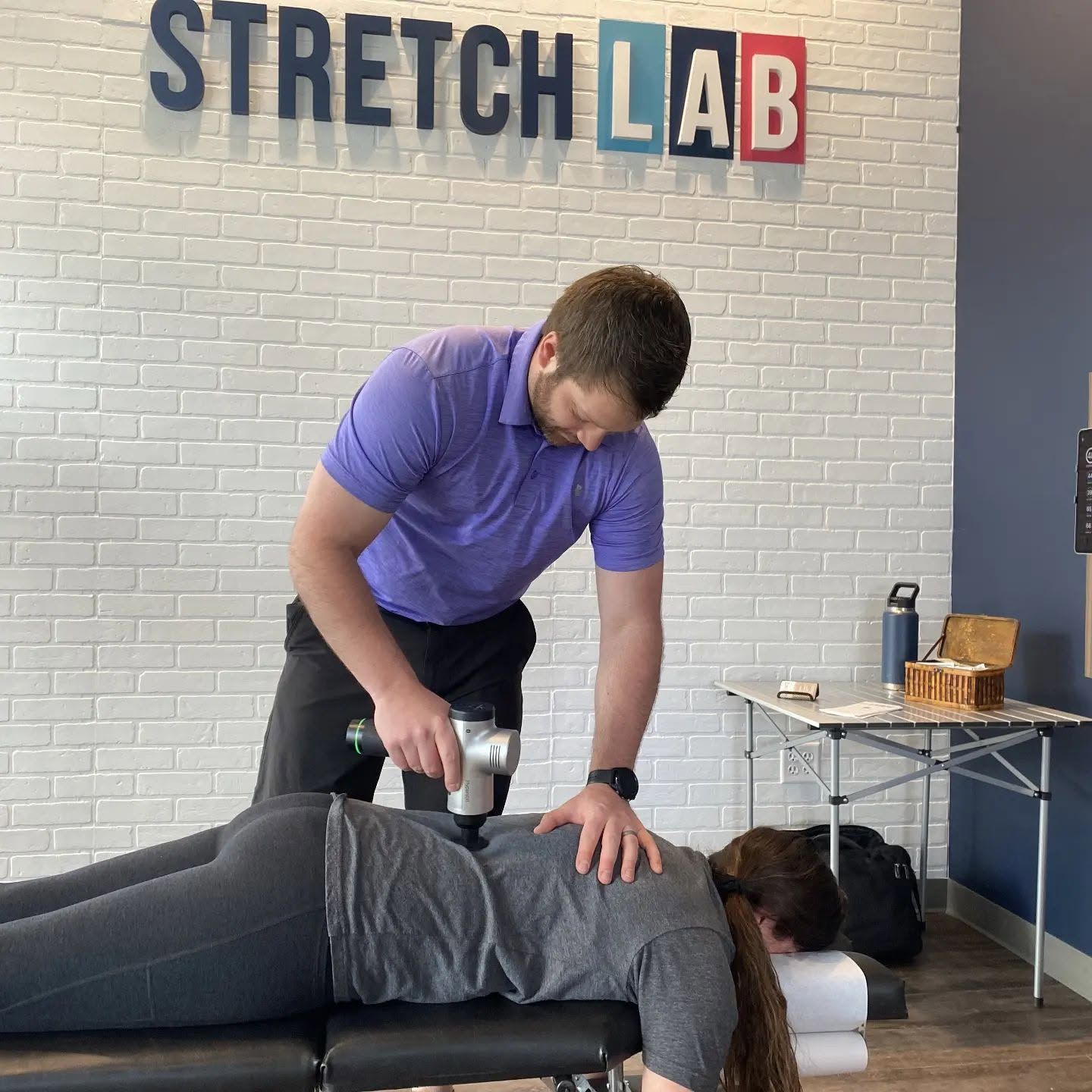 StretchLab therapist using a massage gun on a client lying face down on a treatment table