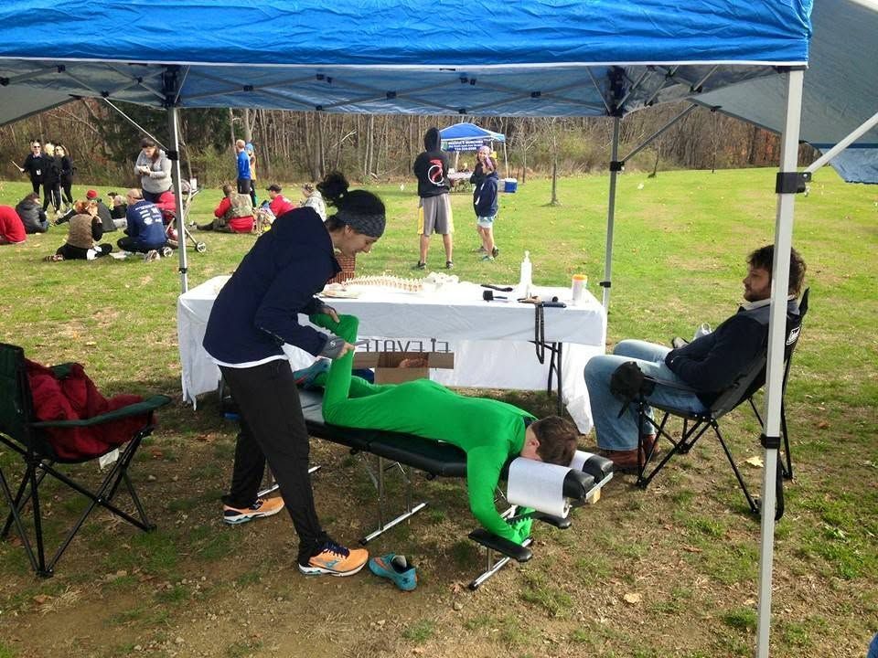 Outdoor event tent with people around a table, one person lying on the grass in a green costume.