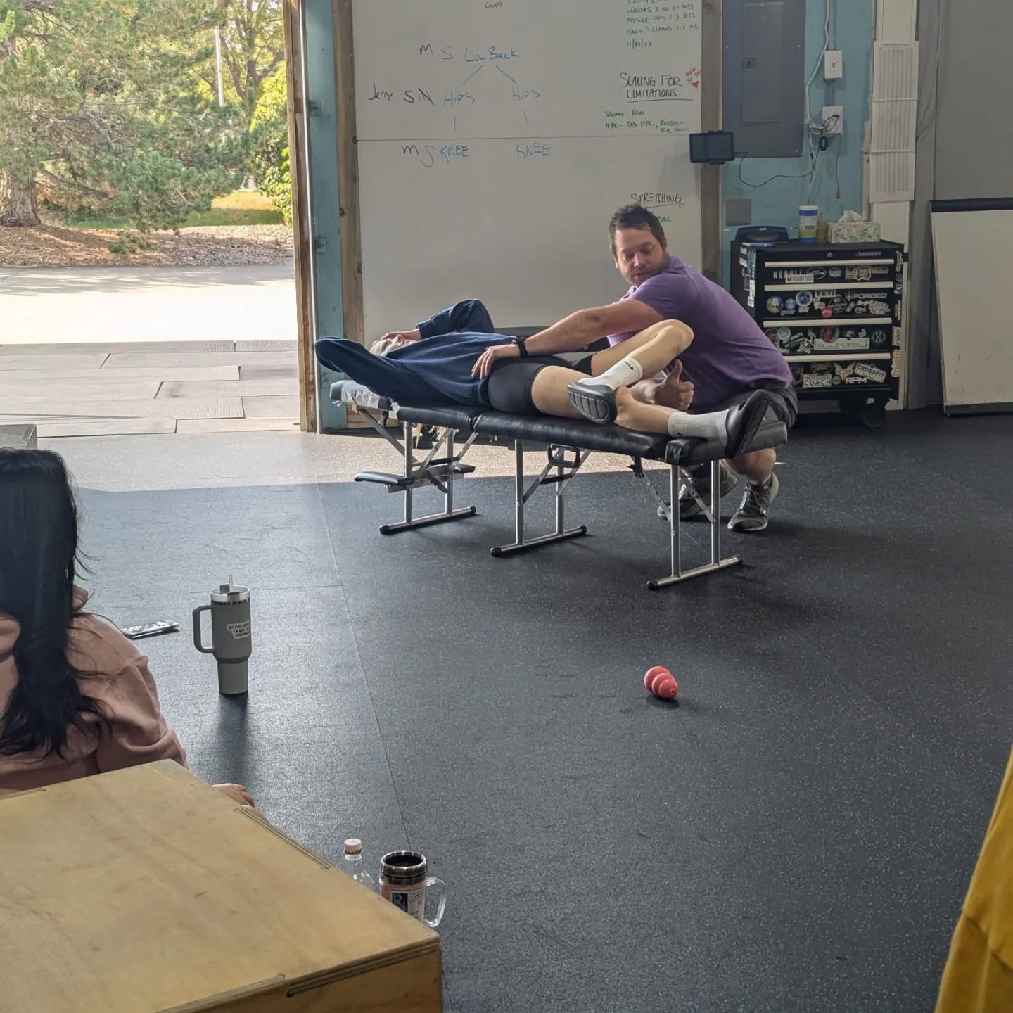Person stretching on low benches in a gym with open garage door and equipment nearby