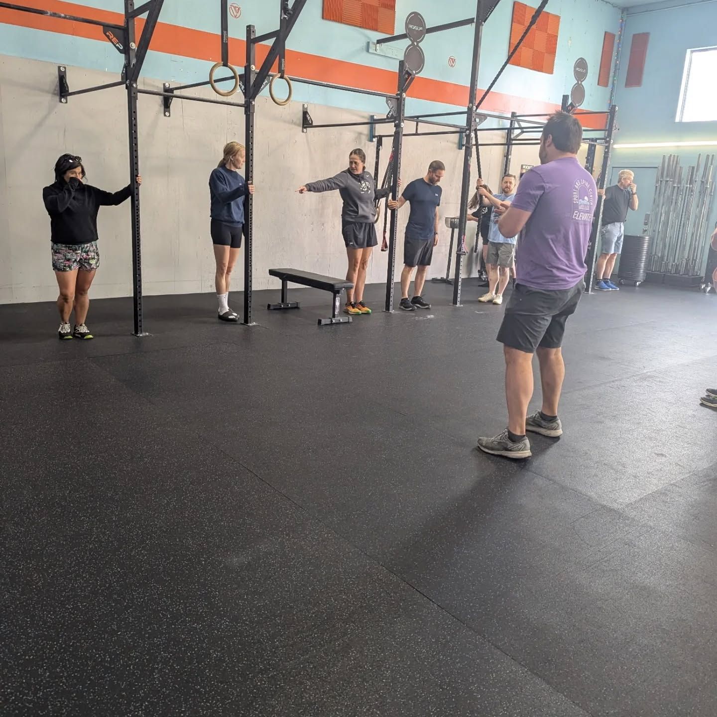 People exercising with pull-up rigs in a gym, viewed from behind on a black floor.