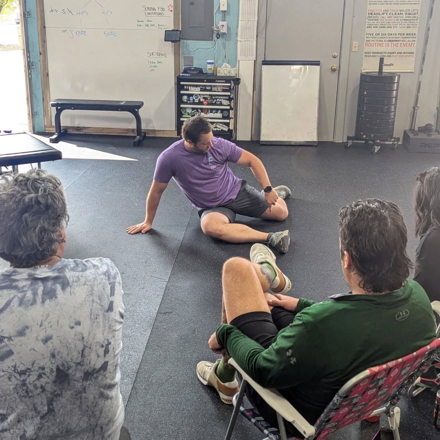 Small group seated on a gym floor, listening to an instructor in a purple shirt