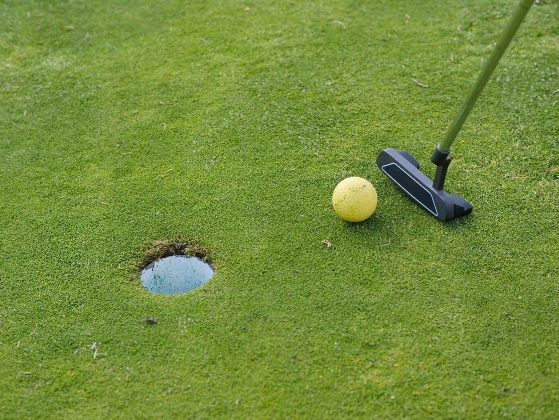 Man putting on a mini-golf course at sunset, holding a putter near a red obstacle.