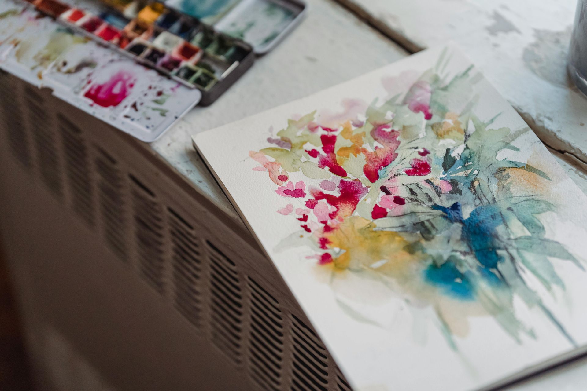 Watercolor artwork on table next to watercolor paint.