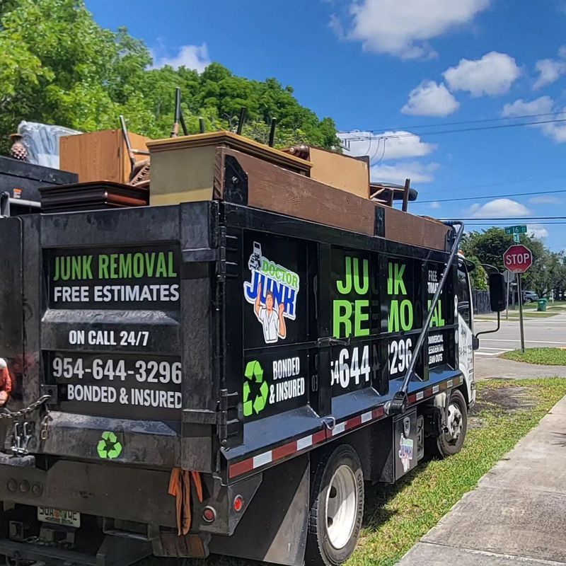 Junk removal truck loaded with furniture, parked by a street. Green and black branding.