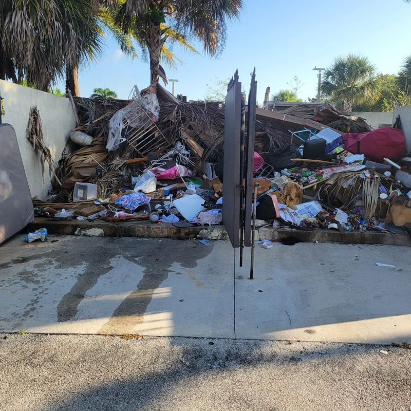Large pile of debris behind a gate, possibly a dumpster. Mostly brown and gray, with some pink items visible.