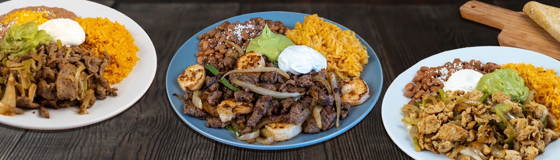Plates of Mexican food, including meat, rice, guacamole, and sour cream. Tortillas and sauces on the side.
