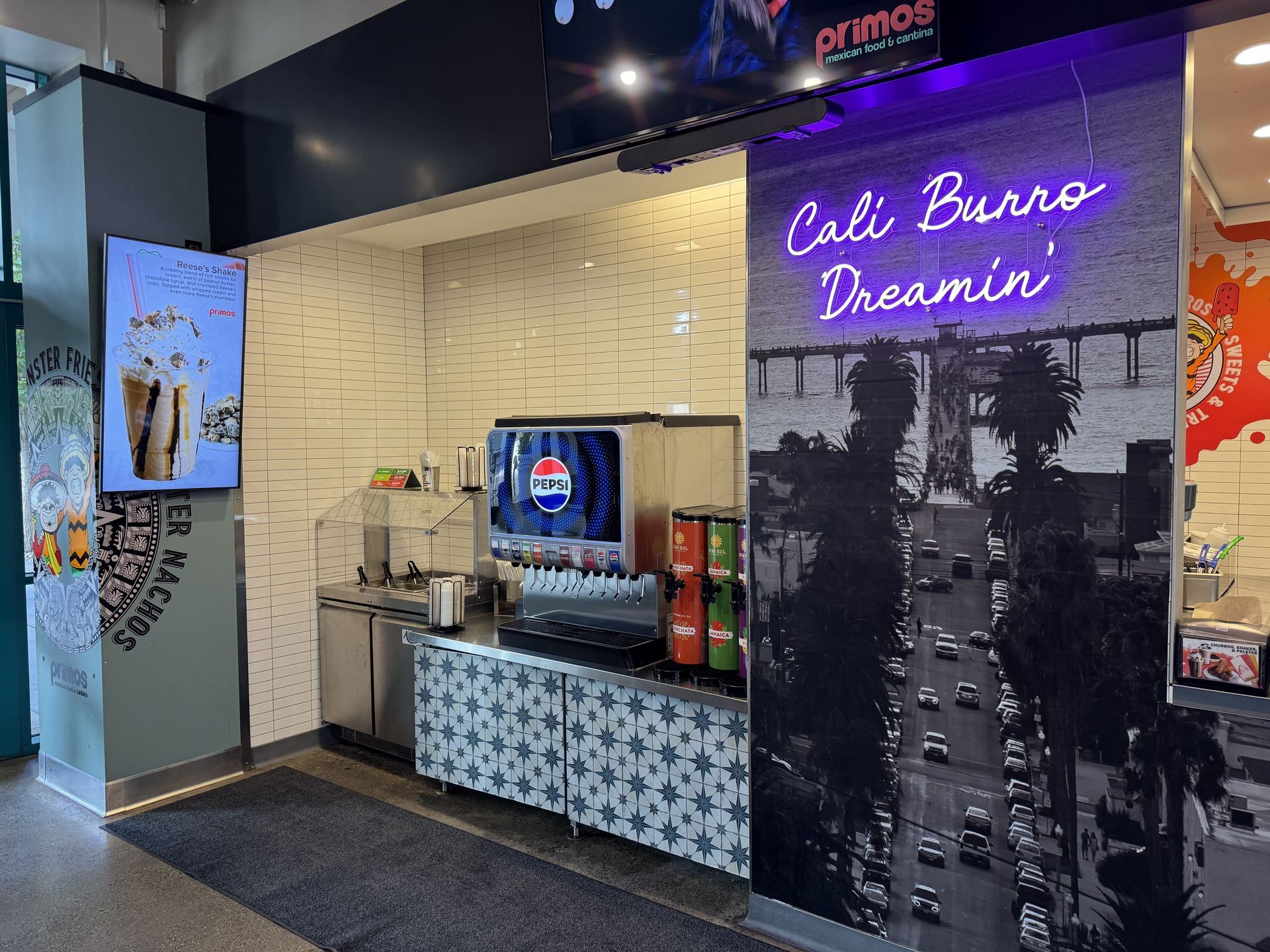 Primos interior featuring a drink station with a Pepsi machine, a mural with neon lights that read