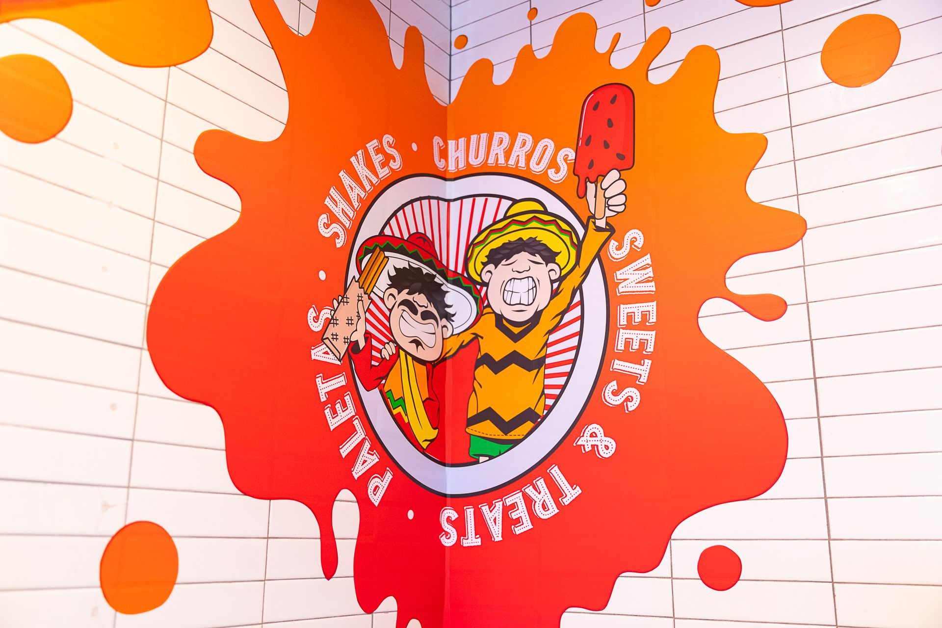 Mural with cartoon figures holding treats, inside an orange splash. Text: 