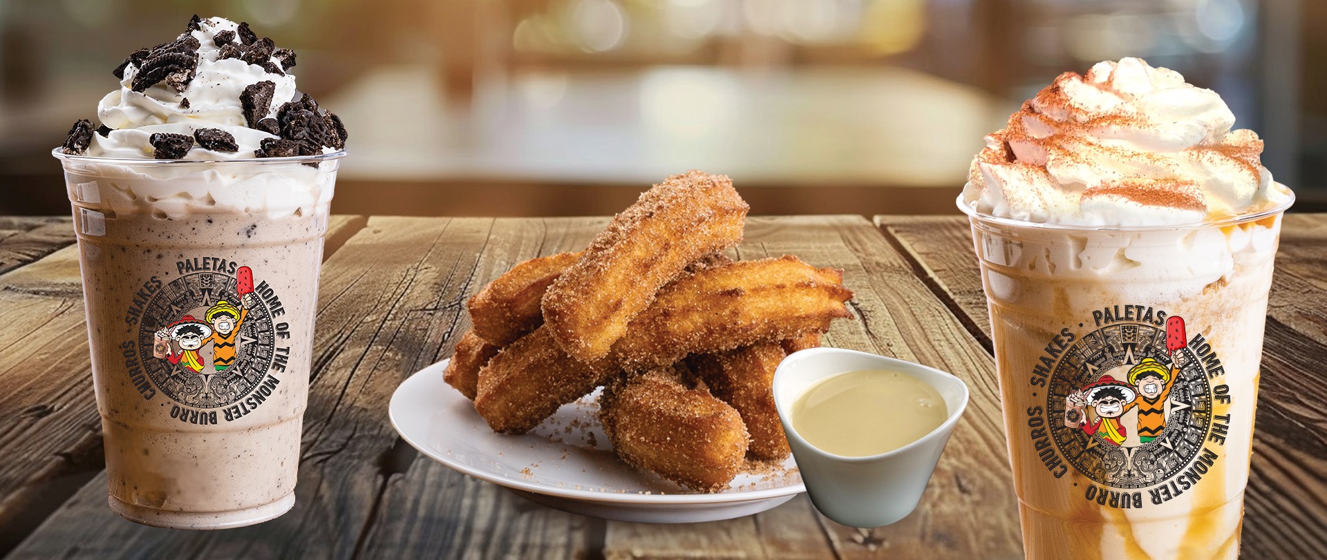 Churros, dipping sauce, and two blended drinks with whipped cream on a wooden table.