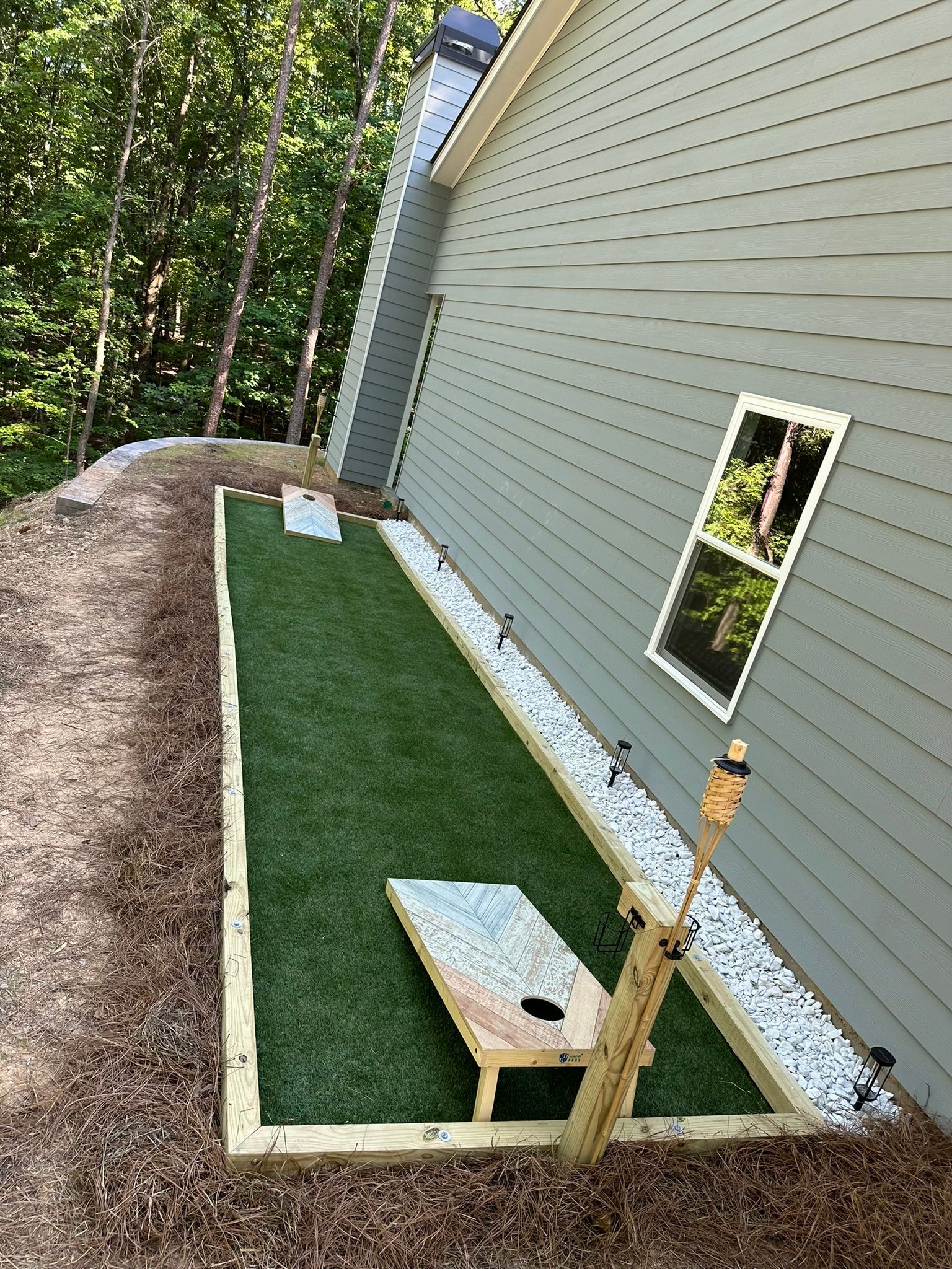 A bag toss game is being played in the backyard of a house.