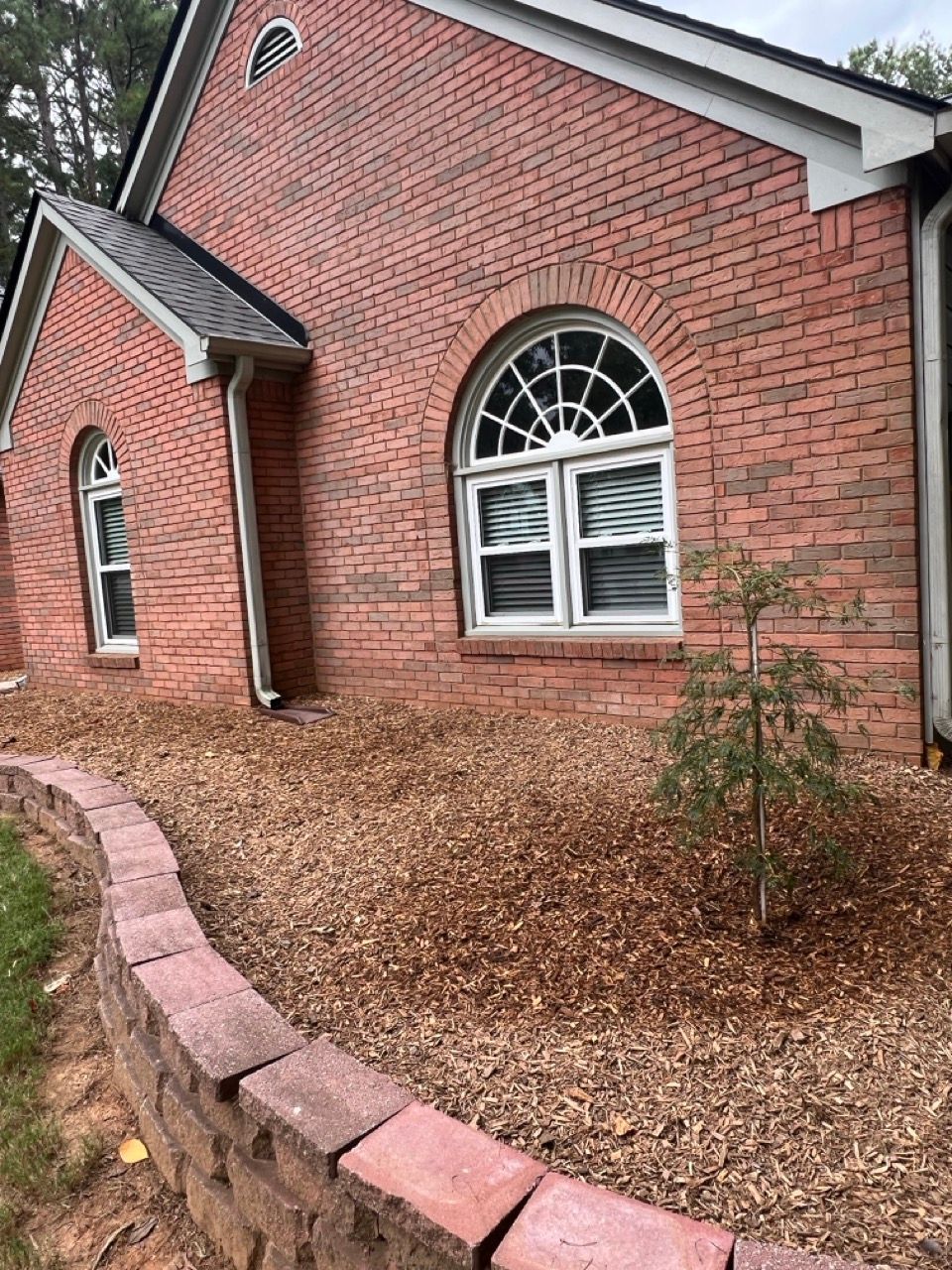 A brick house with arched windows and a brick wall in front of it.