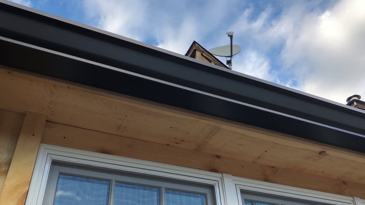 Close-up of a house roof eave with white soffit, black trim, and blue sky above