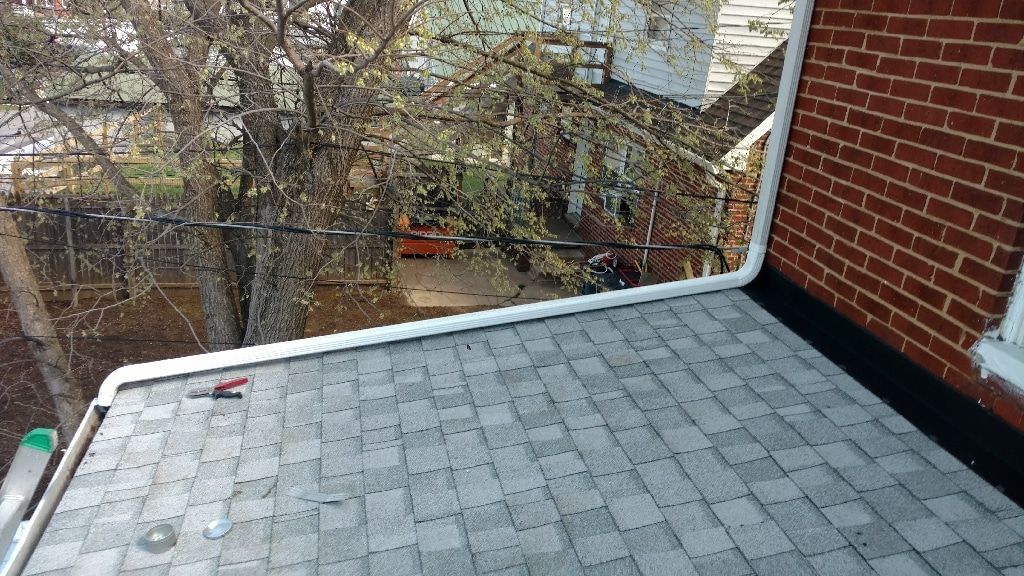 Rooftop with gray shingles beside a brick wall, overlooking leafless trees and neighboring houses